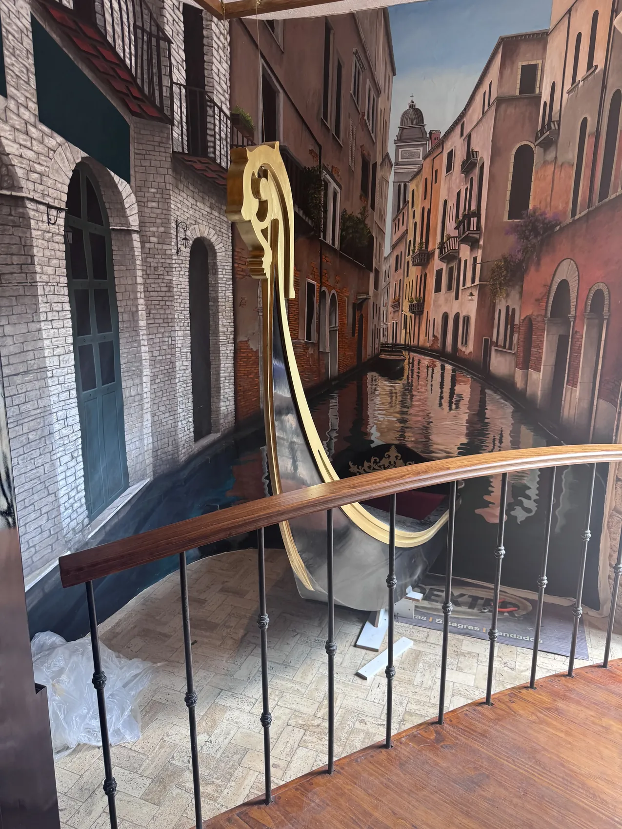 Escalera con barandal de hierro junto al mural del canal y la proa dorada de la góndola.