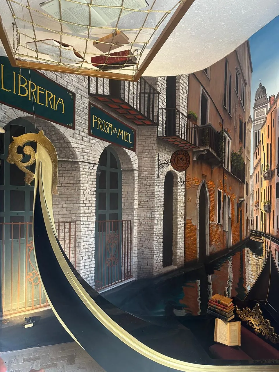 Mural del canal de Venecia pintado en el interior de la librería, con la proa dorada de una góndola y los letreros de LIBRERÍA y PROSA & MIEL sobre arcos de ladrillo.